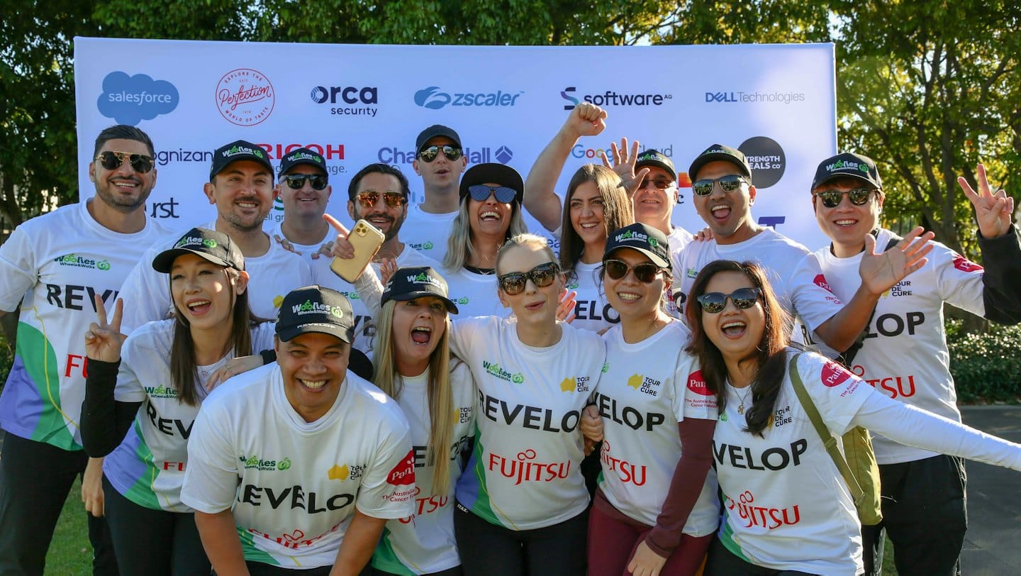 Group of volunteers wearing branded shirts smile at a charity event.