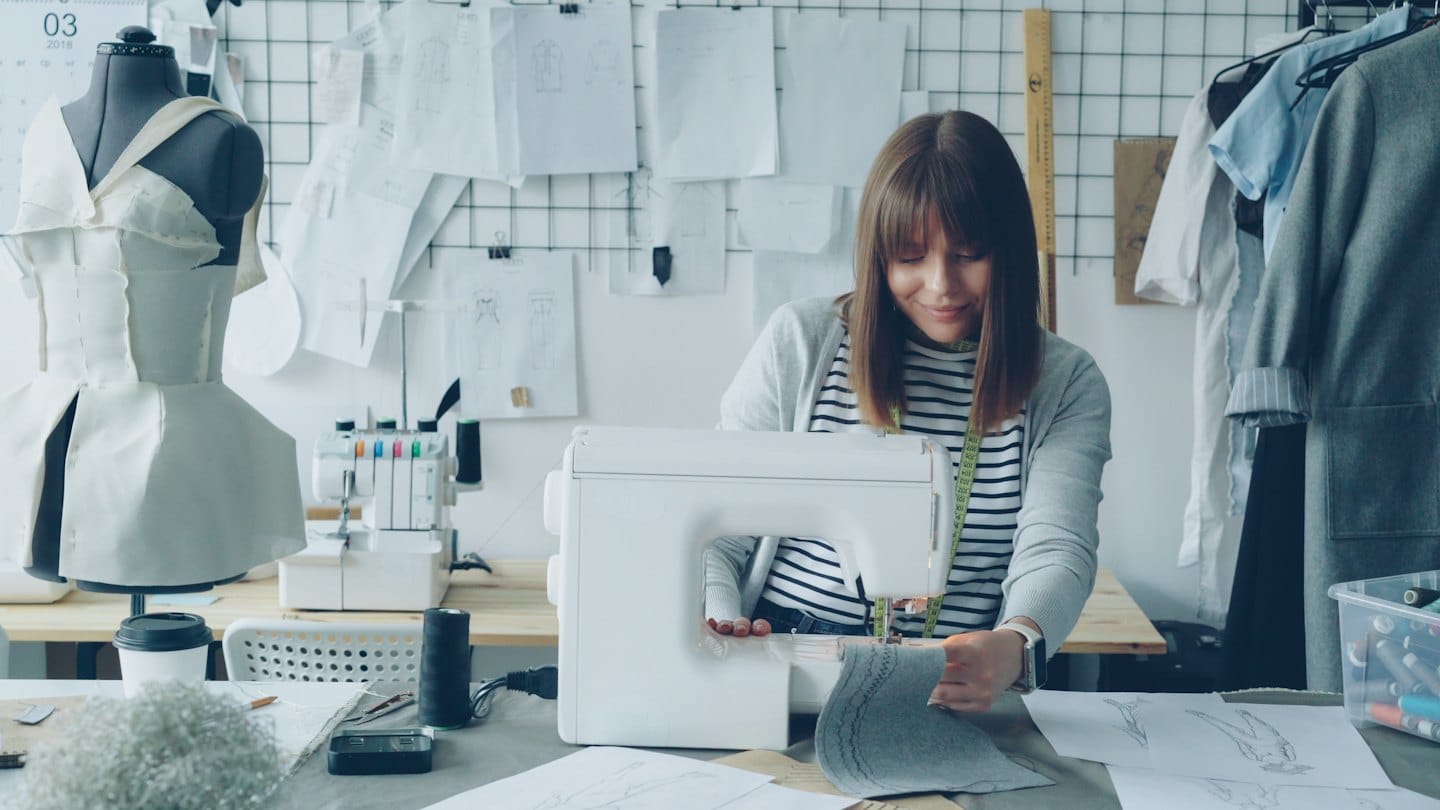 A fashion designer sews grey fabric on a sewing machine.